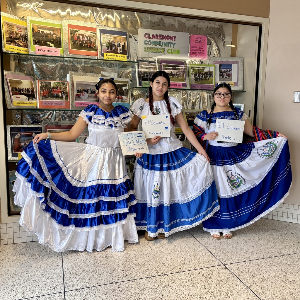 Three young people in traditional El Salvadoran attire stand in front of a display board.
