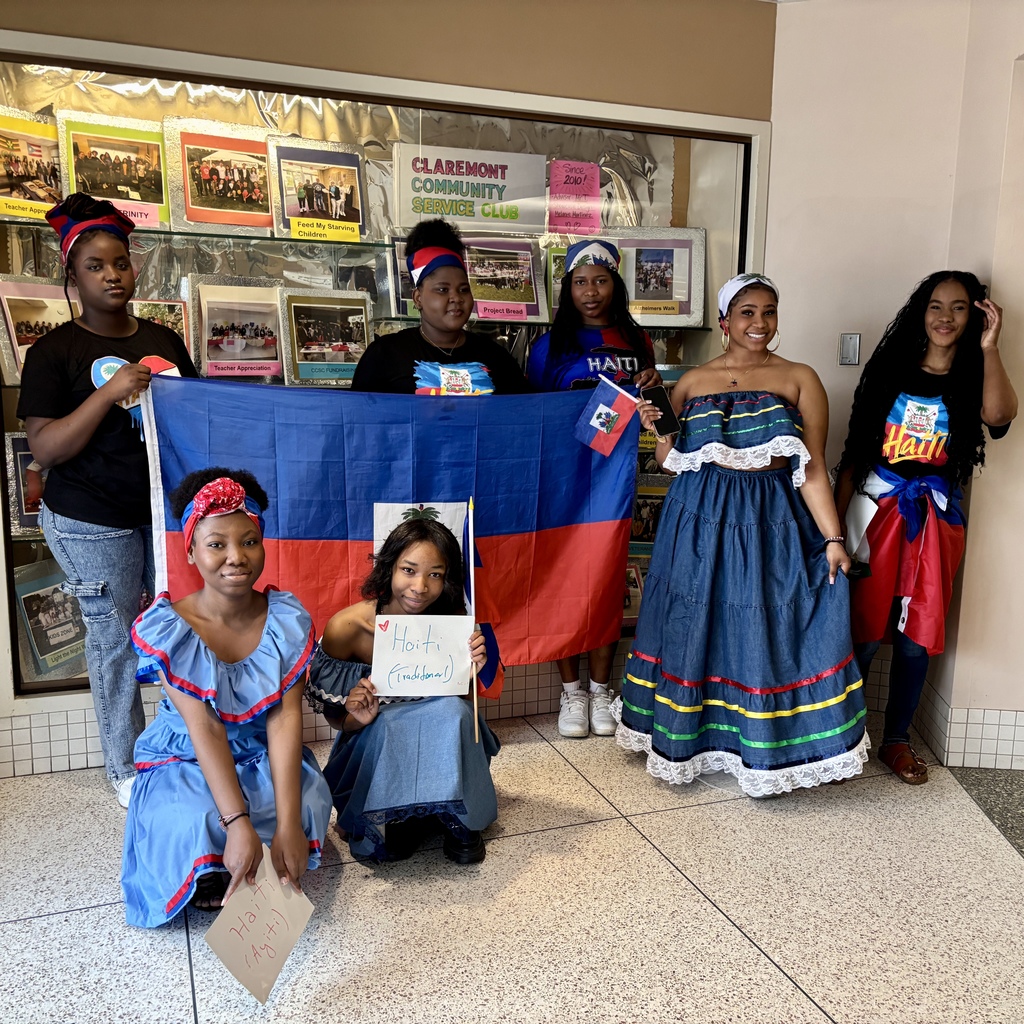 Six young people stand together, holding a large Haitian flag and smaller flags, some wearing traditional attire.