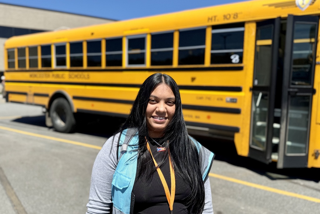 Three individuals stand in front of a yellow school bus with "WORCESTER PUBLIC SCHOOLS" printed on its side.