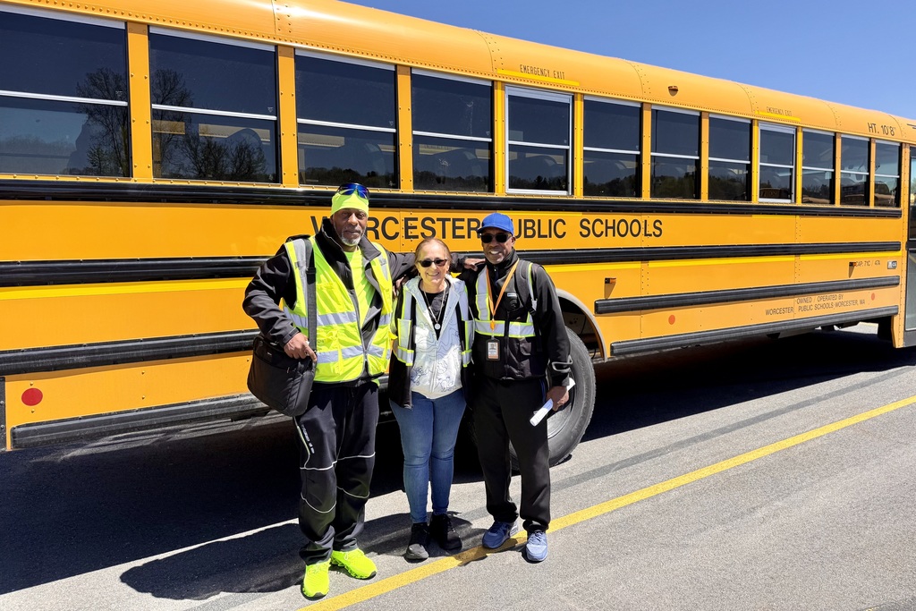 Three individuals stand in front of a yellow school bus with "WORCESTER PUBLIC SCHOOLS" printed on its side.