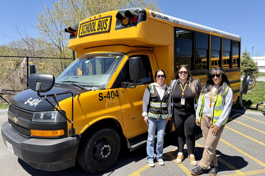 Three women stand in front of a yellow school bus labeled 'S-404' and 'SCHOOL BUS'.