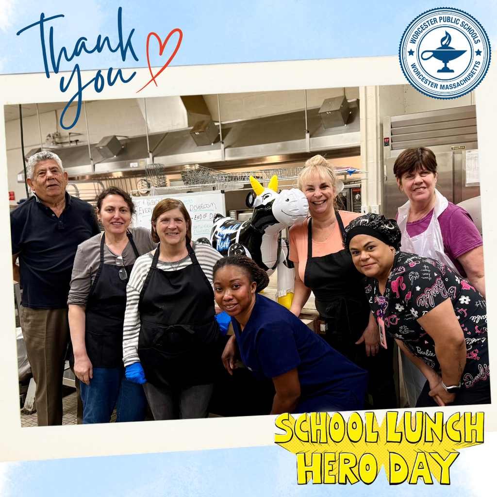 A group of smiling school lunch staff pose for a photo in a kitchen, with a cow balloon and 'Thank You' text.