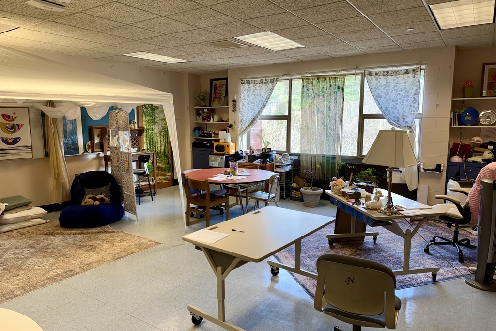 A cozy classroom corner features a white tent, beanbag chair, and stacked pillows on a patterned rug.