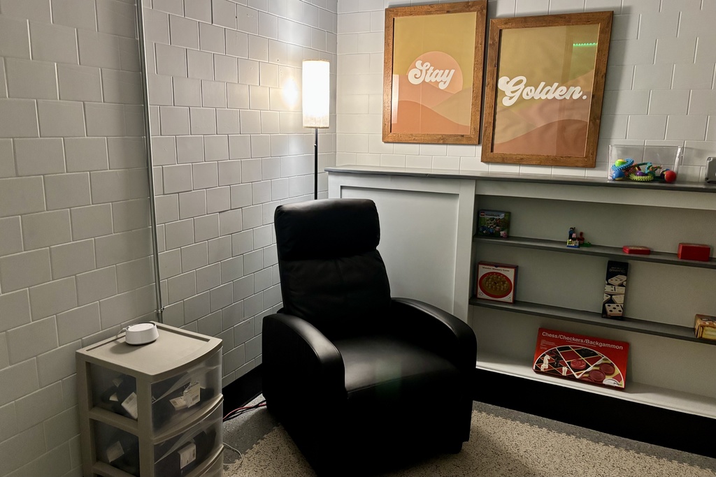 A black recliner chair sits next to a floor lamp in a room with tiled walls.