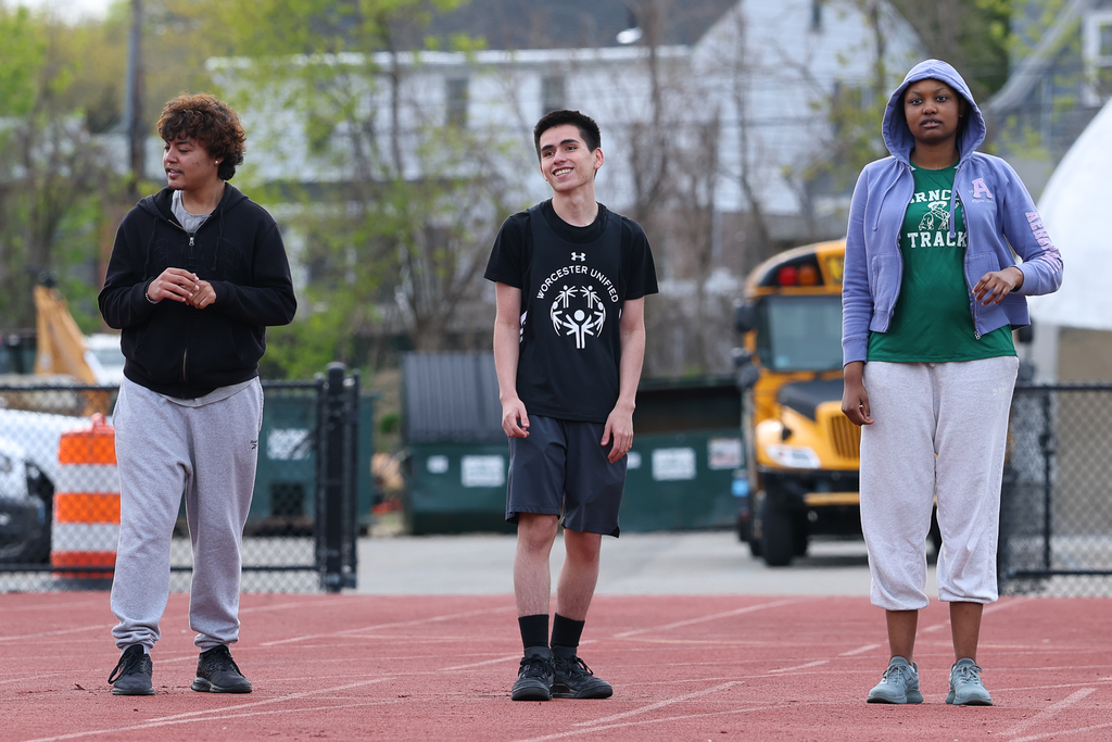 Three students stand at the starting line, one in the middle is smiling.