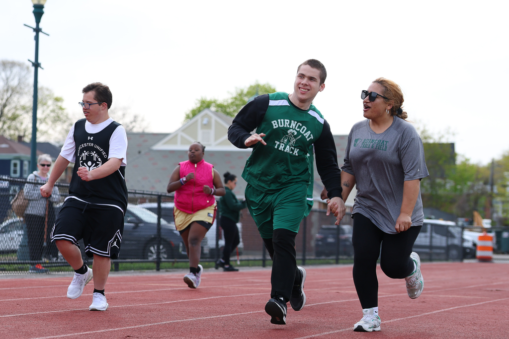 A student runs down the track while holding the hand of a staff member, who is running alongside and cheering them on.