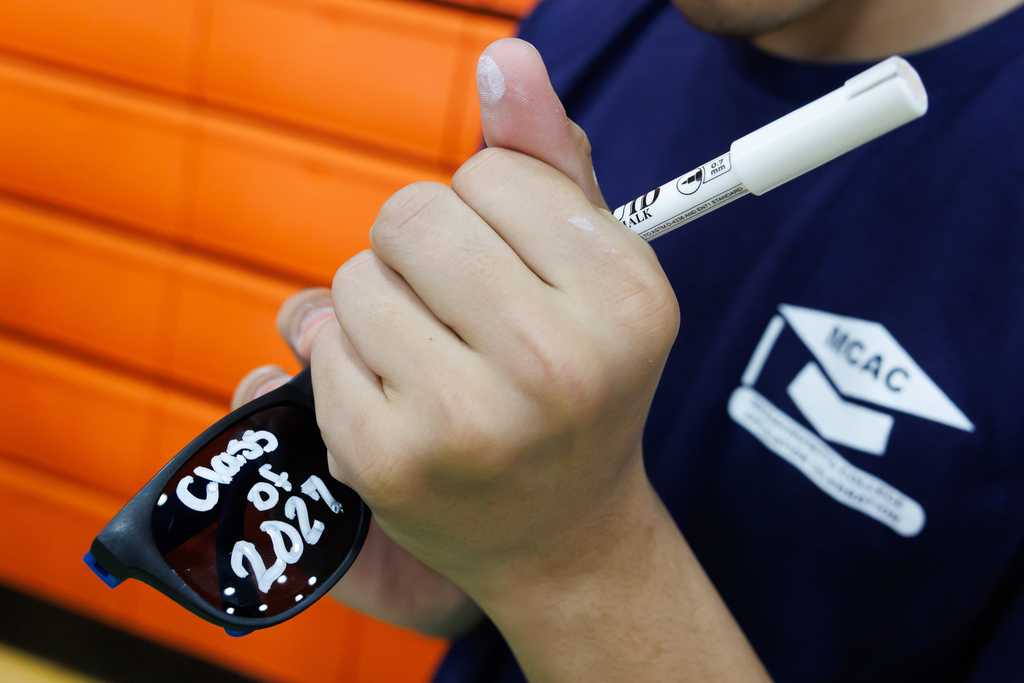 A student writes "Class of 2027" in white marker on black sunglasses.