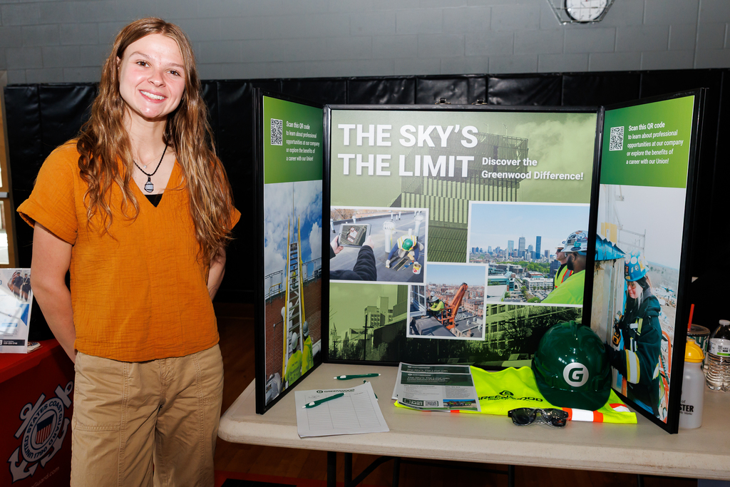 A representative of Greenwood Industries stands besides a poster board presentation during a career fair.