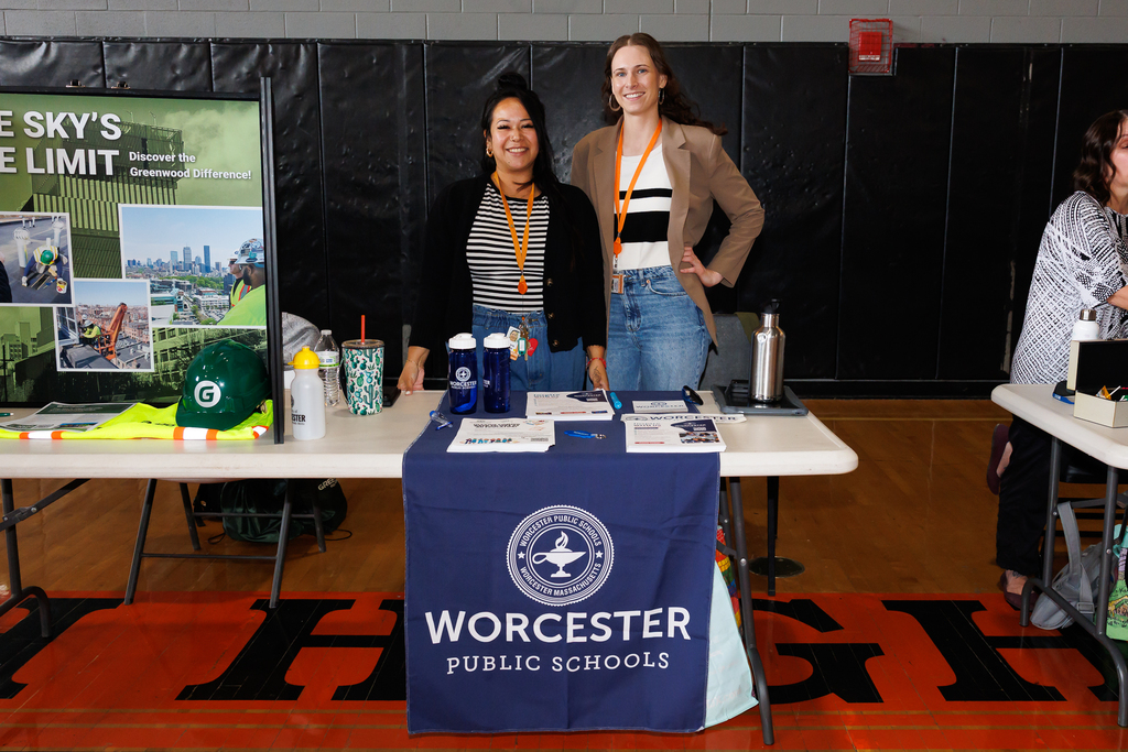 Representatives from Worcester Public Schools stand behind a table draped with the Worcester Public Schools logo.