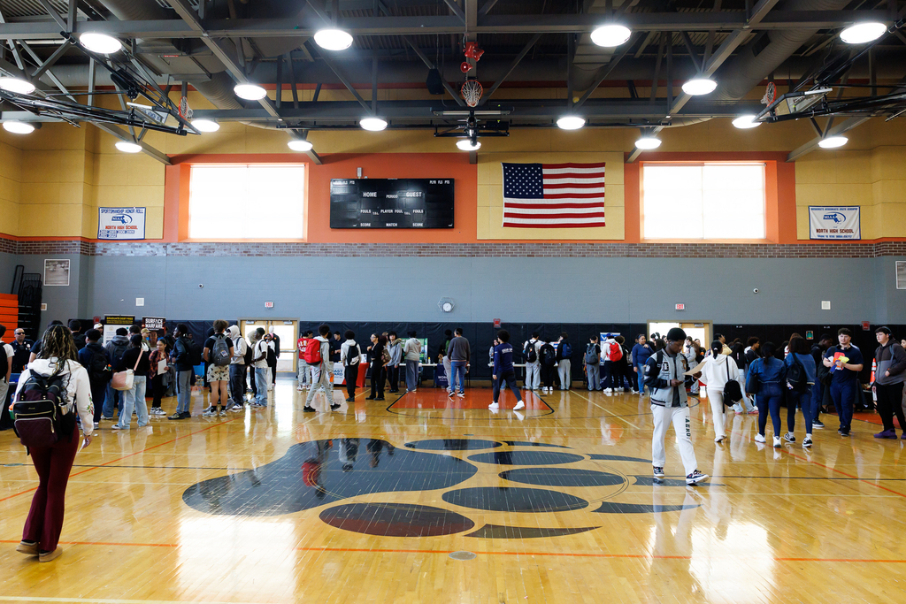 A wide image of the gymnasium during a career fair with students and businesses scattered around the area.