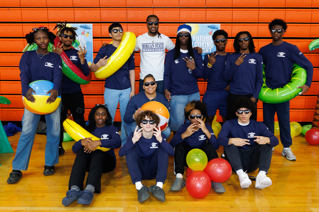 A group of students stand with a teacher during a career day, holding beach themed props.