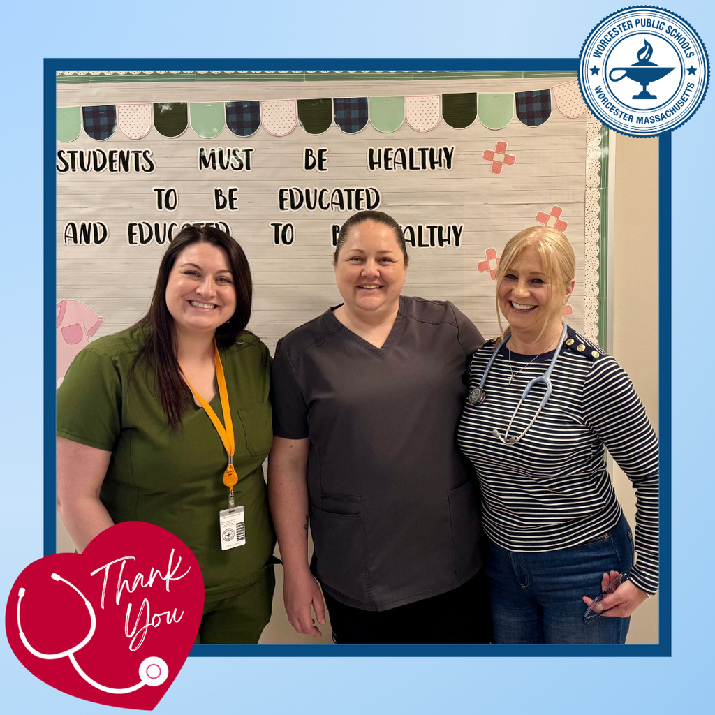 Three smiling women in scrubs and casual wear stand in front of a bulletin board with text about health and education.