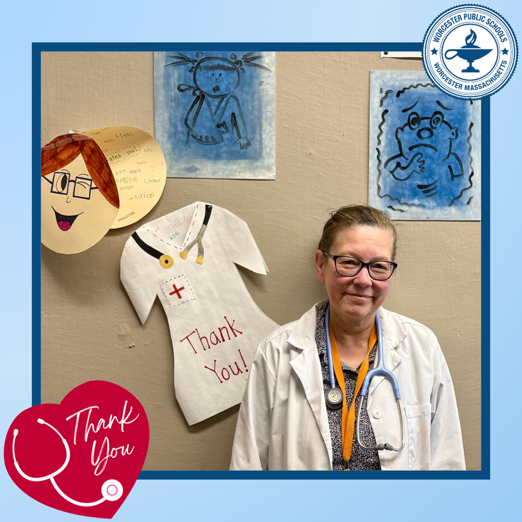 A healthcare professional smiles, standing in front of children's artwork thanking them.