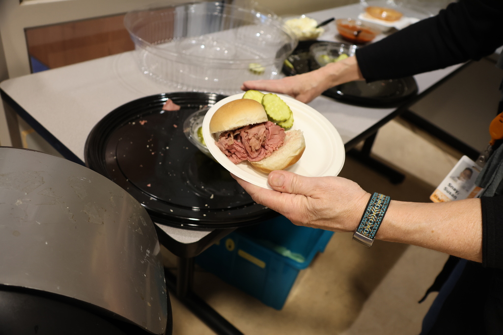 A person holds a plate with a roast beef sandwich and pickles, preparing to serve.