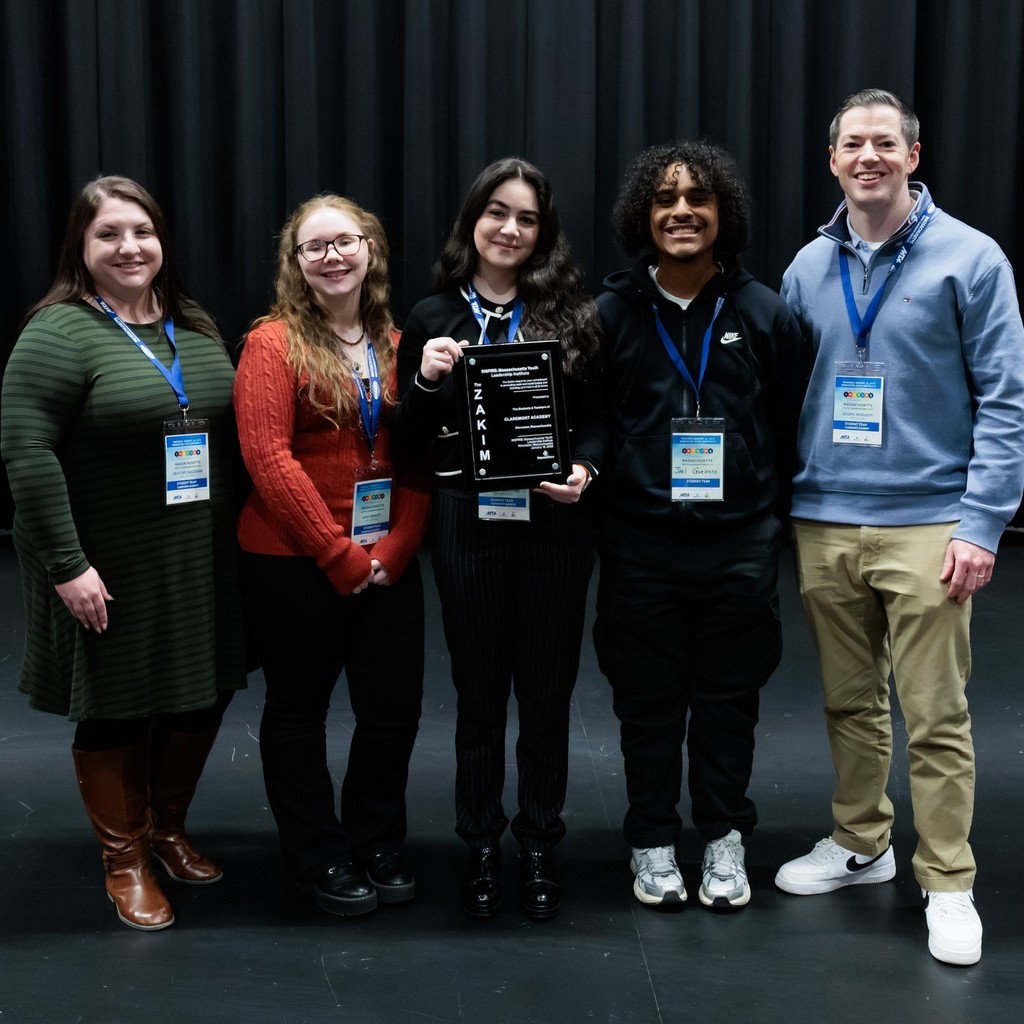Five individuals, including three young adults and two adults, pose for a photo with a plaque.