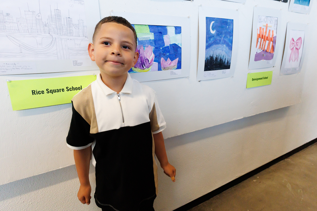 A student smiles while standing in front of their artwork.