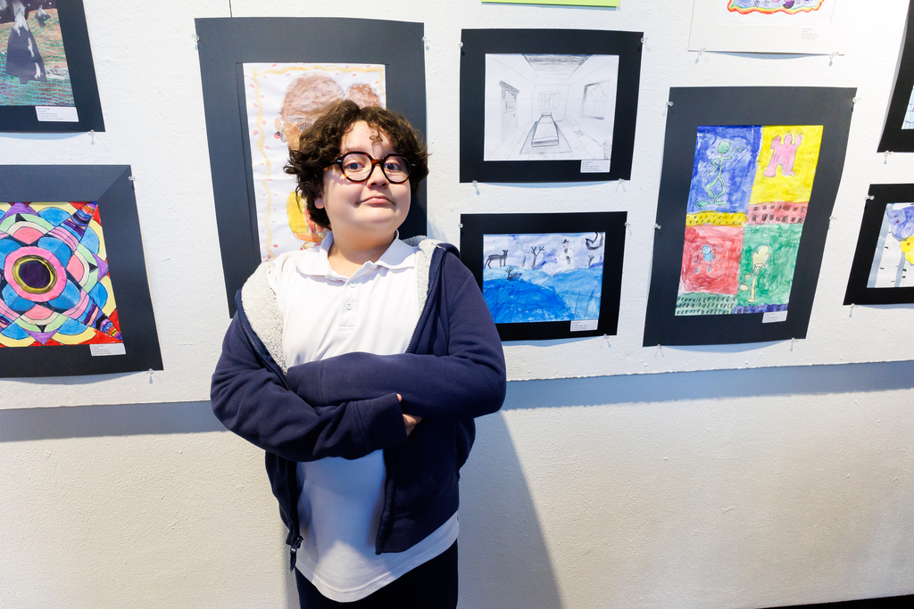 A student crosses their arms while standing near their artwork.