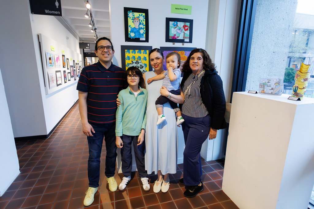 A family of five stands together proudly in front of the artwork of their young student.
