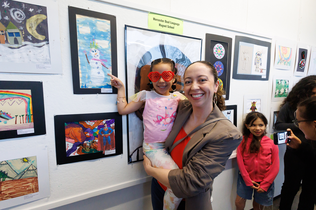 A parent holds up their child while they point at a piece of artwork on display.