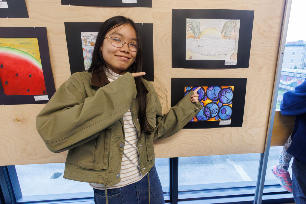 A student points at their artwork on display.