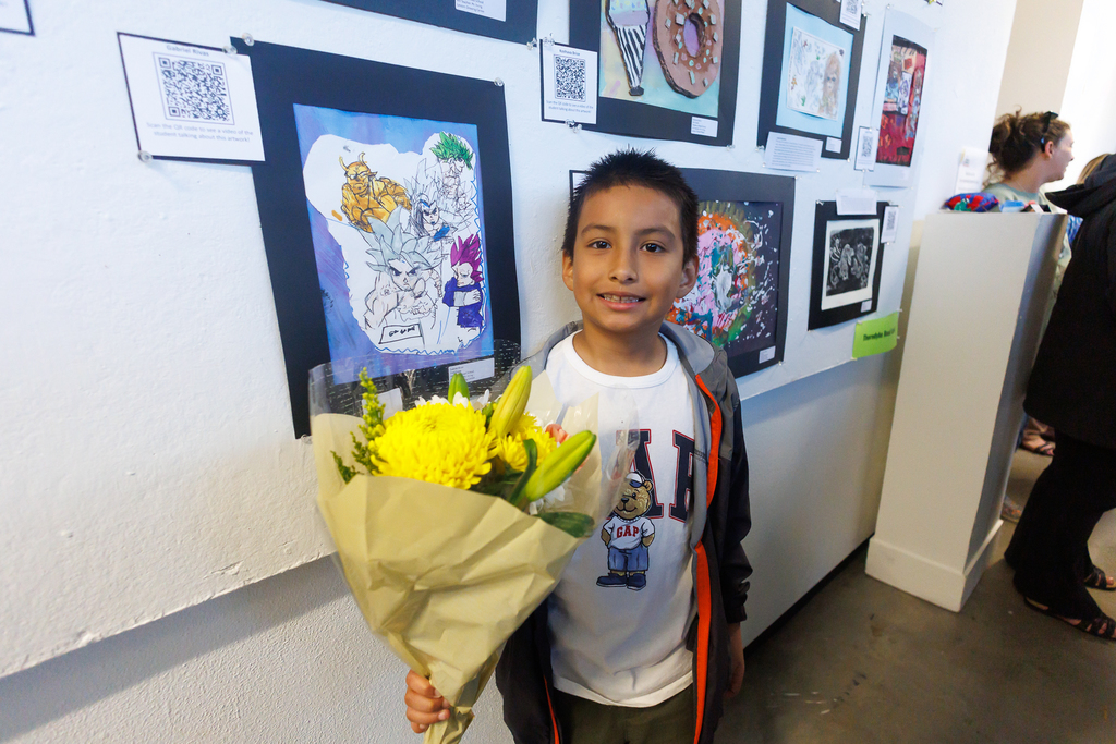 A student stands in front of their artwork while holding flowers.