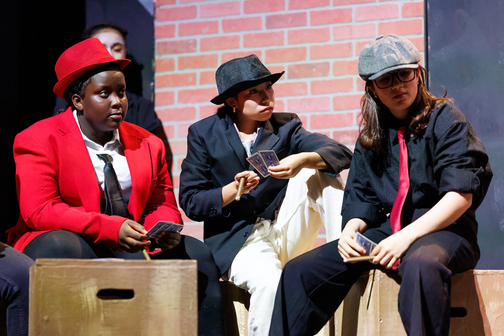 Three students wearing hats and suit jackets act on stage.