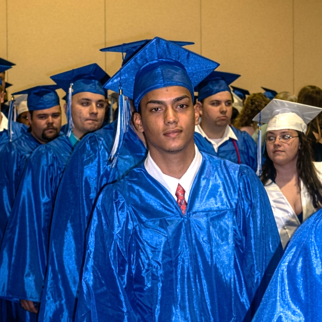 A group of graduates in blue gowns and caps stand in a line, anticipating their ceremony.
