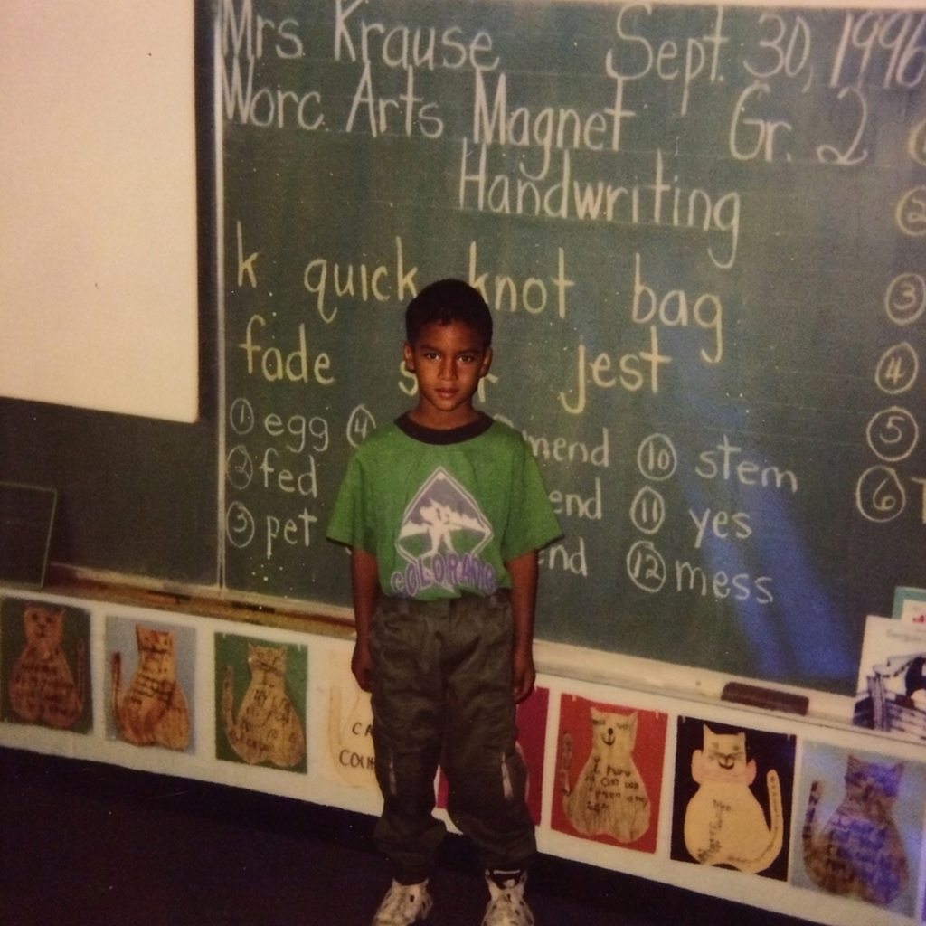 A young boy stands in front of a chalkboard with the date Sept. 30, 1996, and 'Gr. 2' written on it.