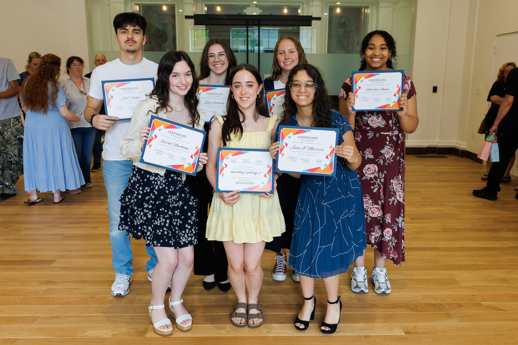 Seven students stand together holding up their award certificates. 