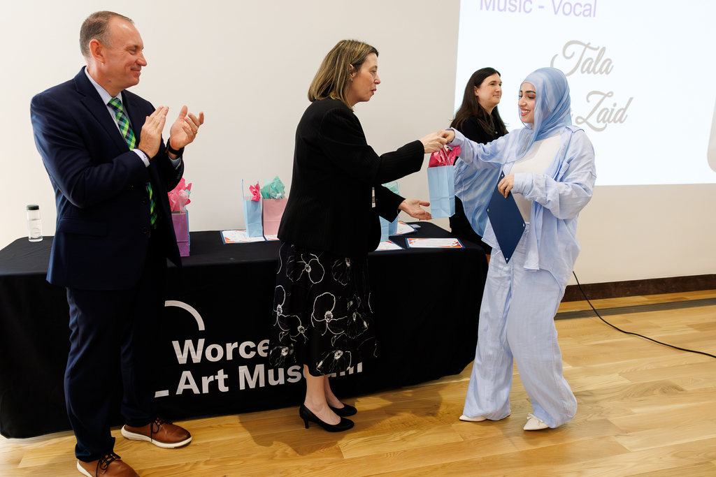 A student accepts a gift bag while adults clap nearby.