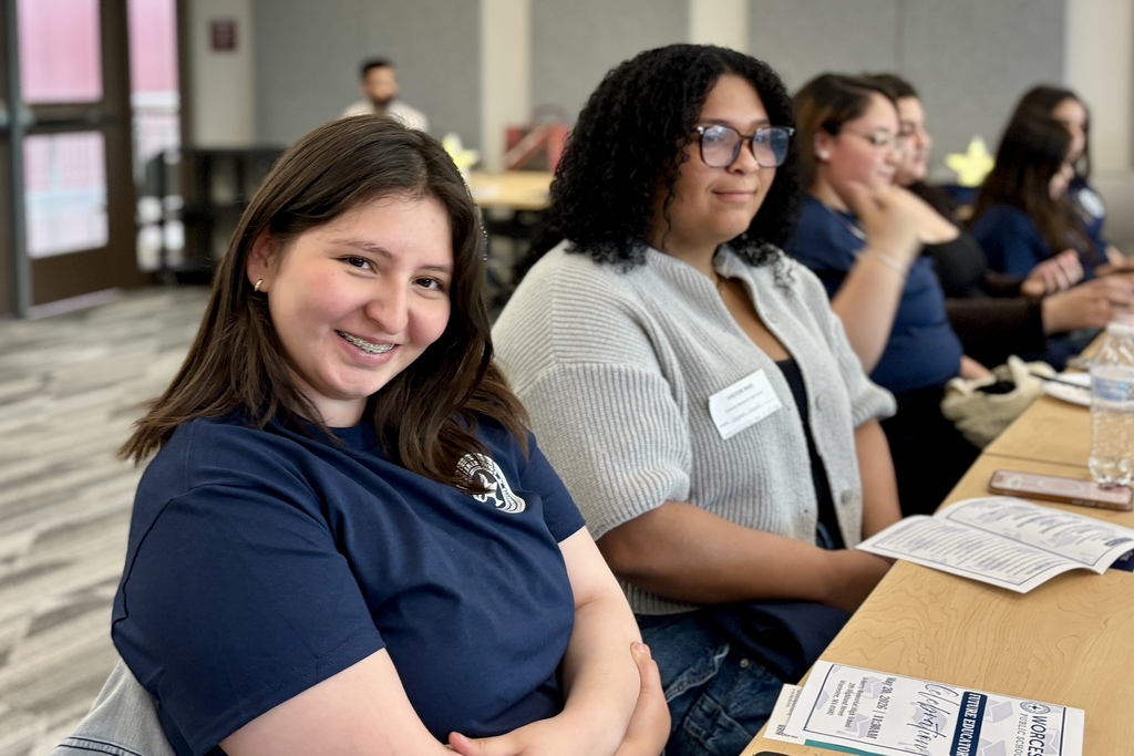 A young woman with braces smiles at the camera while sitting at a table with others.