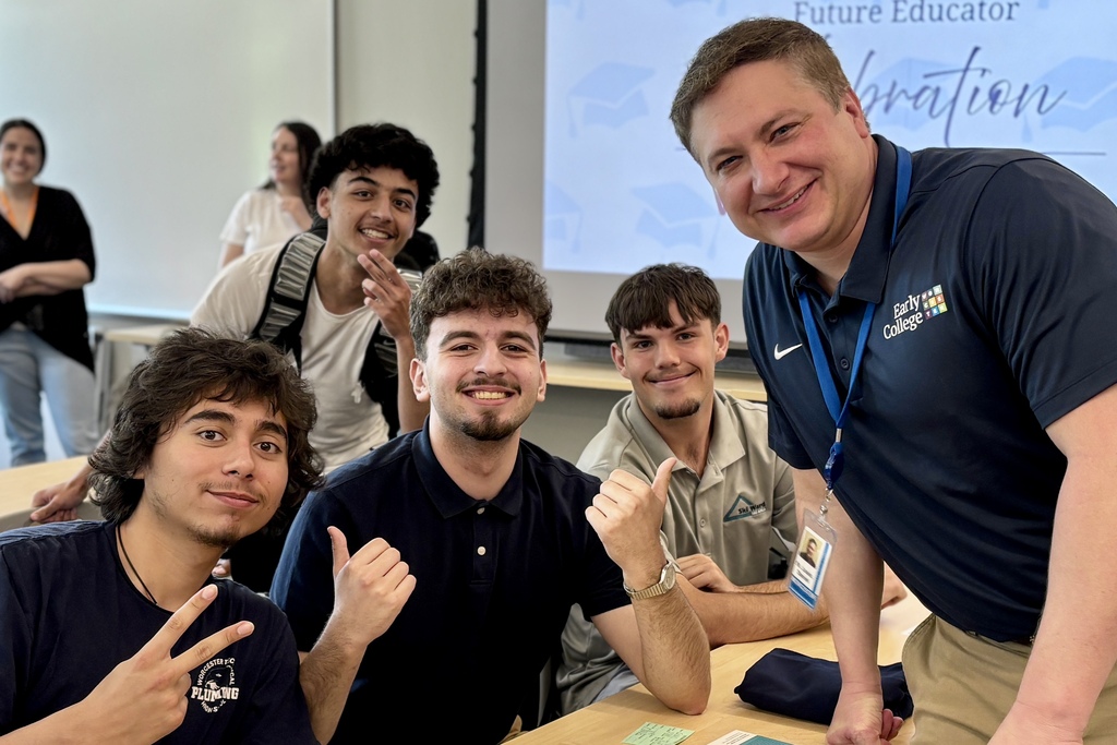 A group of smiling young men and an adult man pose for a photo in a classroom setting.