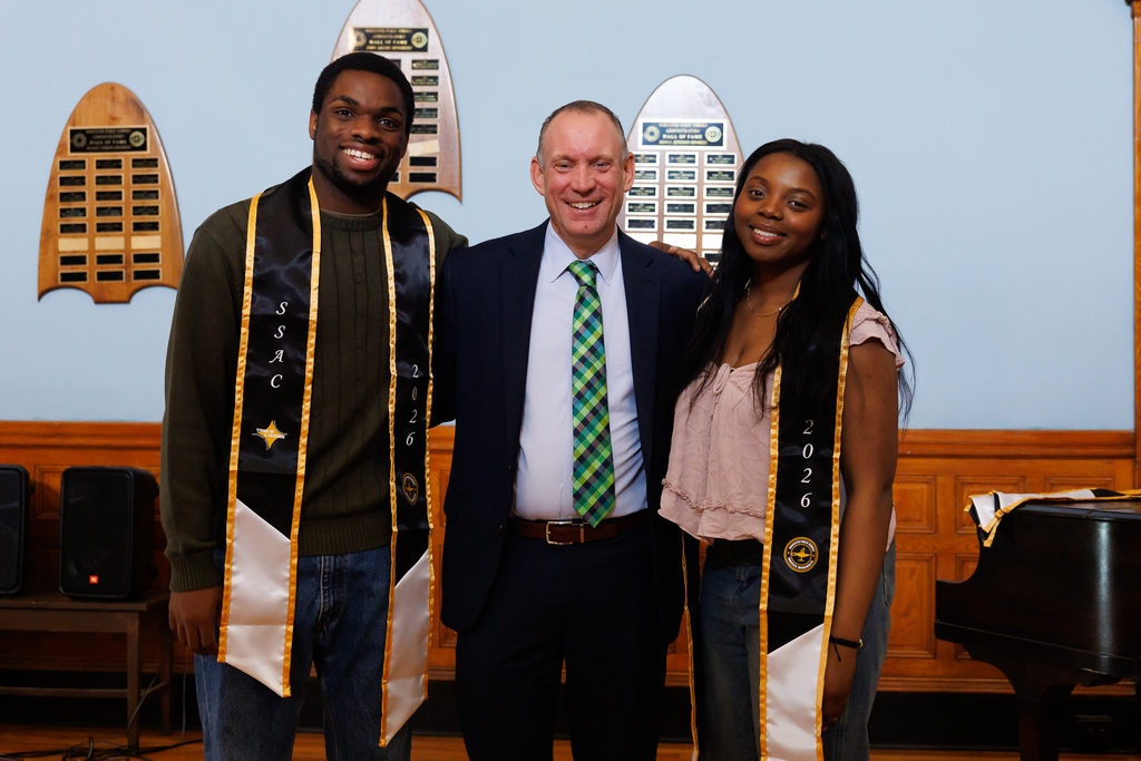 Three students stand beside Superintendent Allen on stage.