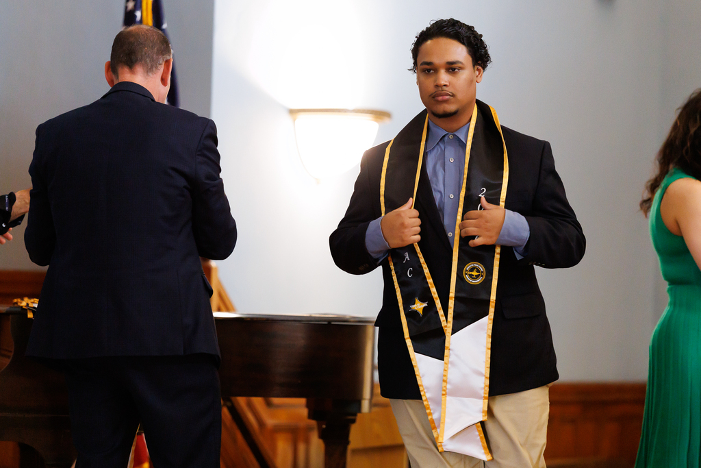 A student adjusts their sash while walking across stage.