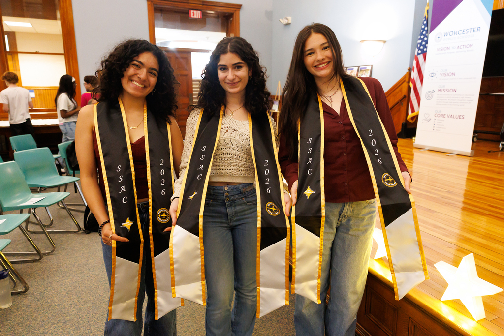Three students smile for a photo while pulling their graduation sash.