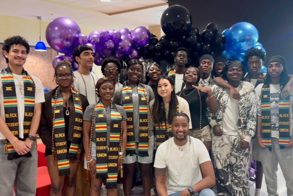 A diverse group of students and an adult pose for a photo, many wearing sashes that say 'Black Student Union'.