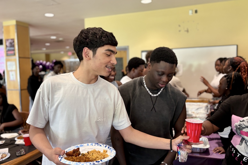 Young people gather around a table with food and drinks at an indoor event.