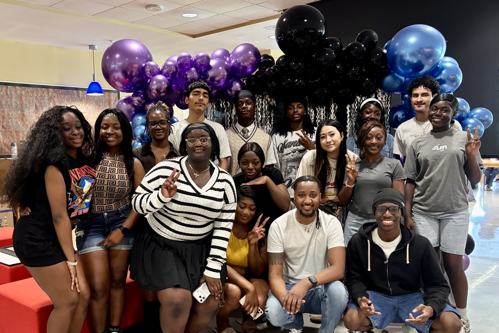 A diverse group of young adults poses for a photo in front of a balloon arch of purple, black, and blue.