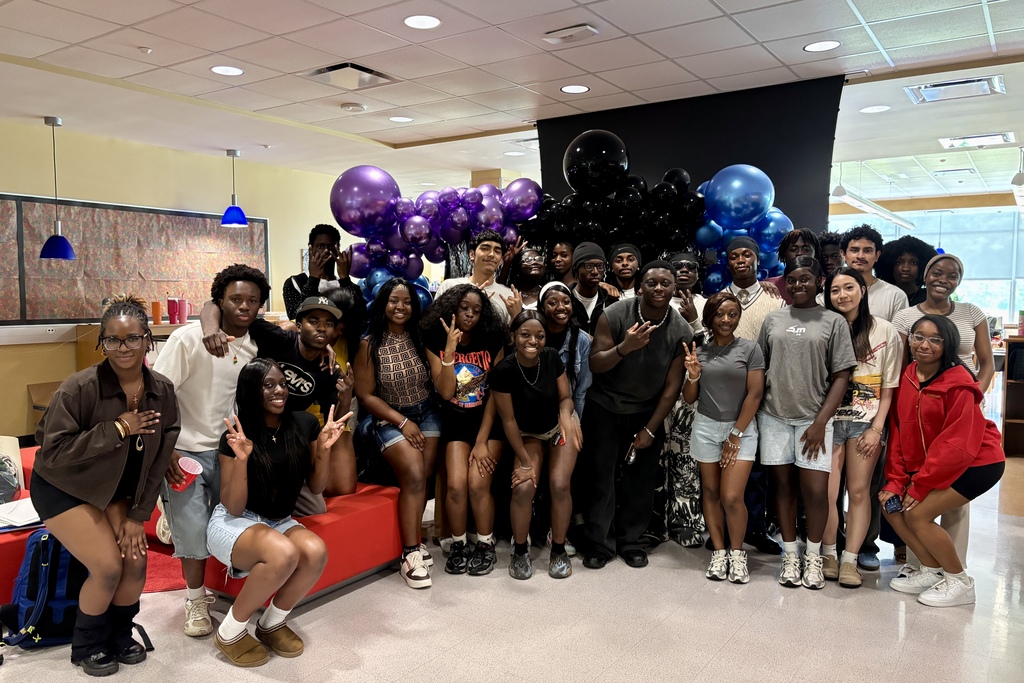 A diverse group of young people pose for a photo in front of a balloon arch.