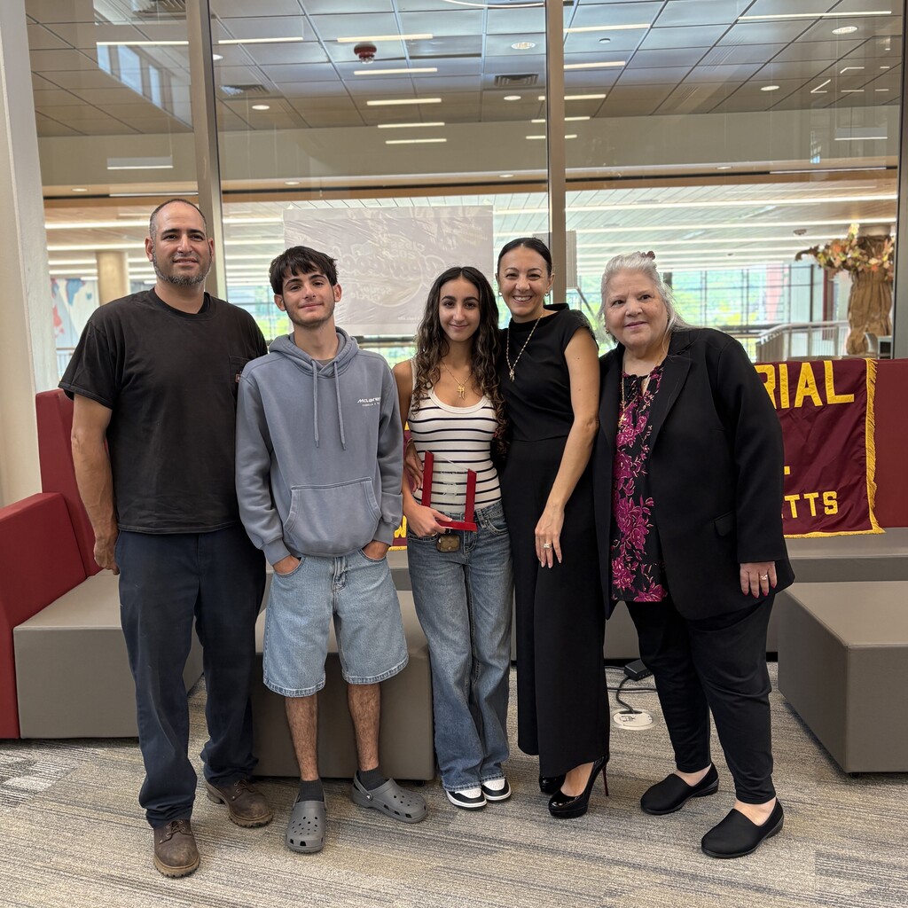 Five people, including two young adults and three adults, pose for a photo indoors.