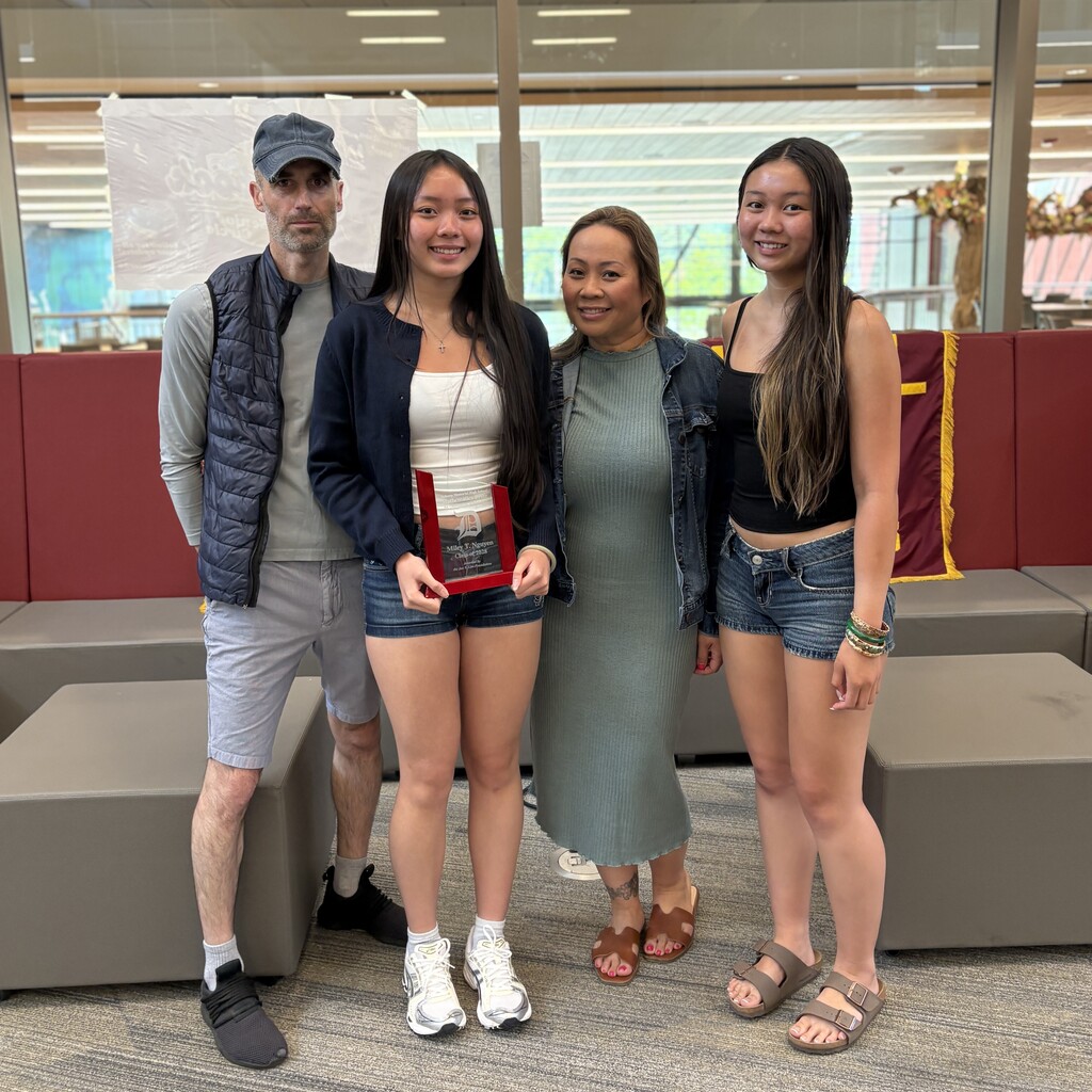 A family poses for a photo, with one daughter holding an award.
