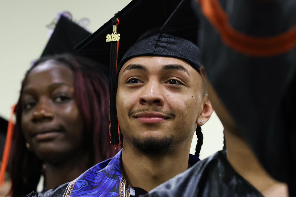 A student smiles while wearing a graduation cap and gown.