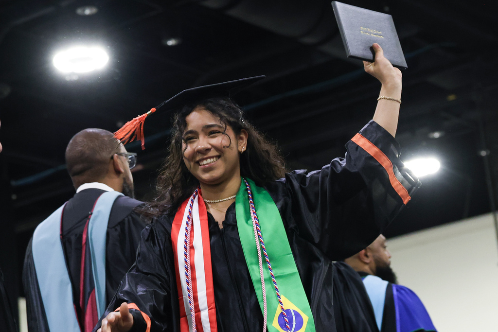 A student raises their diploma while walking across stage during graduation.
