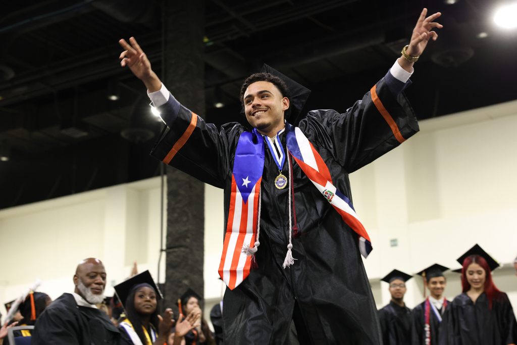 A student raises their arms as they walk across stage at graduation.