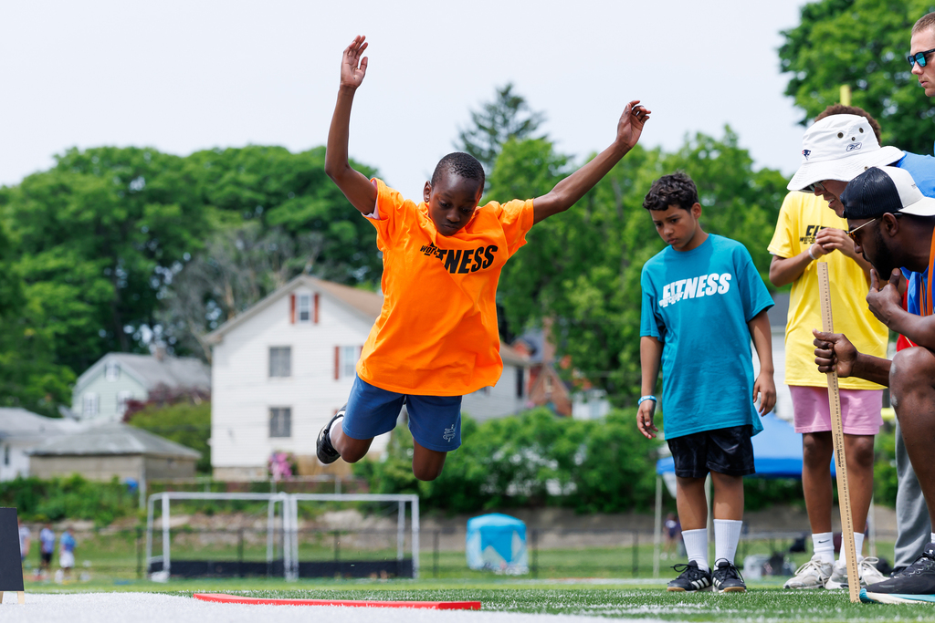 A student leaps while extending their arms during a standing long jump.
