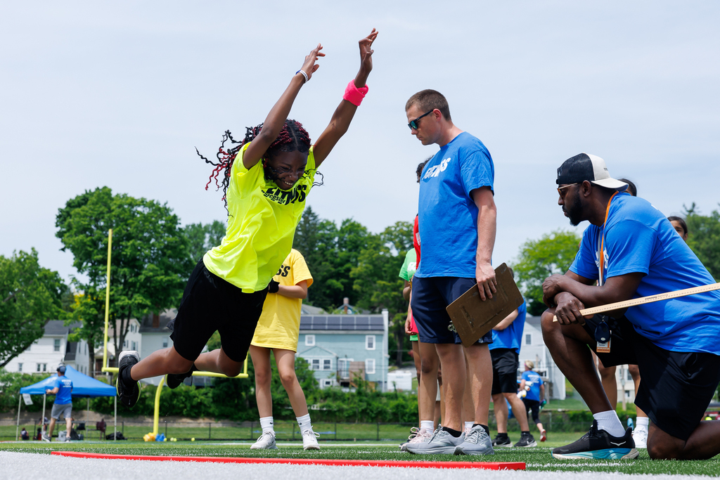 A student leaps while extending their arms during a standing long jump.