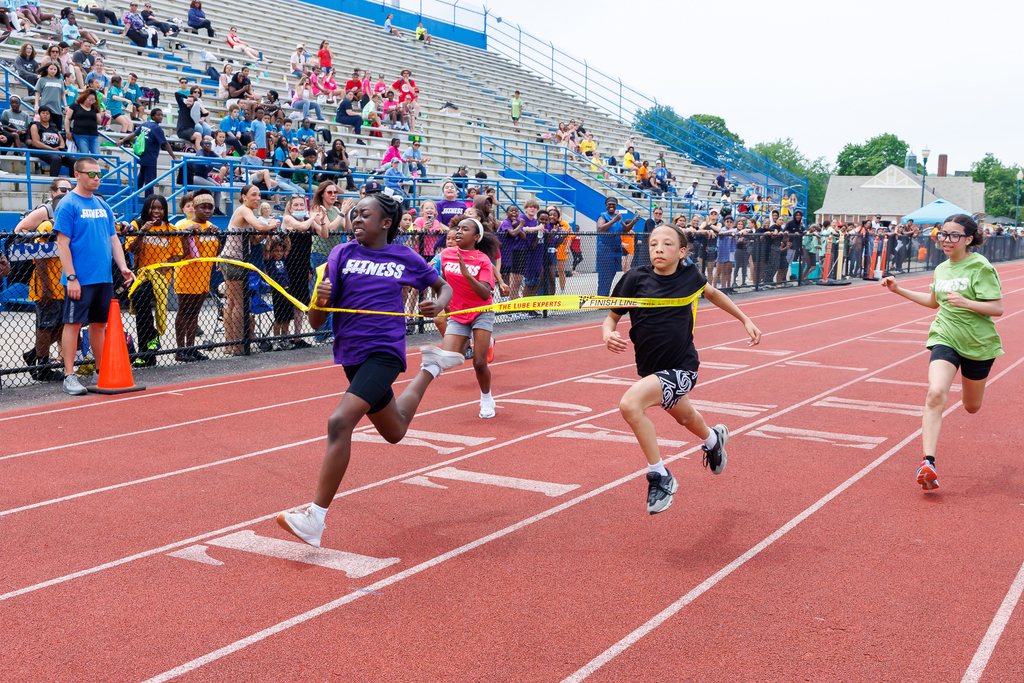 A student runs through the tape during a race with others closely behind.