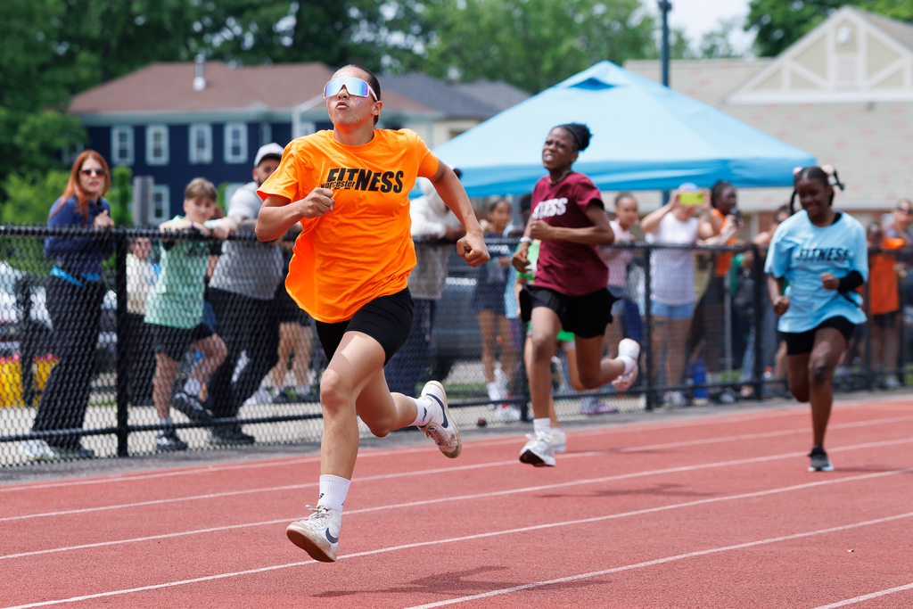 A student runs on the track during a race with two others closely behind.