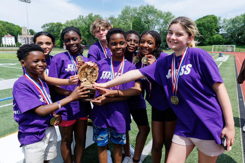 A group of students all put their hand on a trophy after winning an athletic competition.