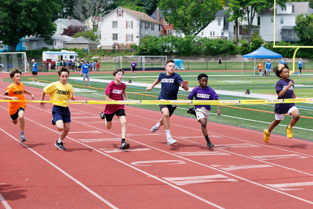Six students run side by side on a track before reaching the tape in a closely contested race.